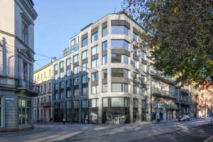 Großes Bürogebäude mit zahlreichen Fenstern, umgeben von Straßeninfrastruktur, Fahrzeugen, Fußgängern, Bäumen und einem bewölkten Himmel, das als neue Hauptverwaltung dient.
